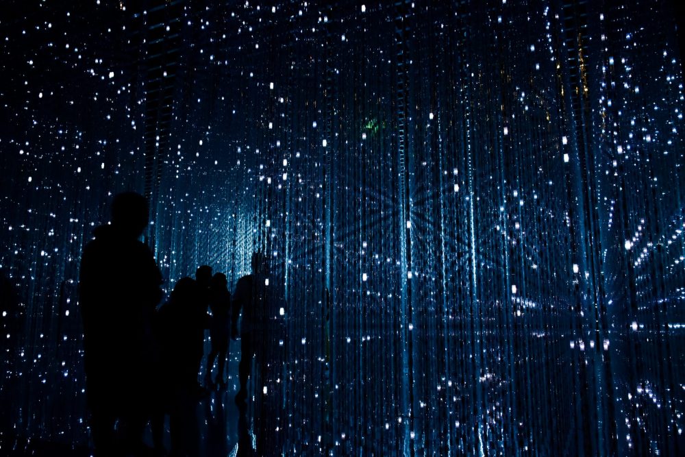 Silhouettes of people standing inside an immersive data visualization installation with cascading blue and white lights representing AI compute and digital infrastructure demand.